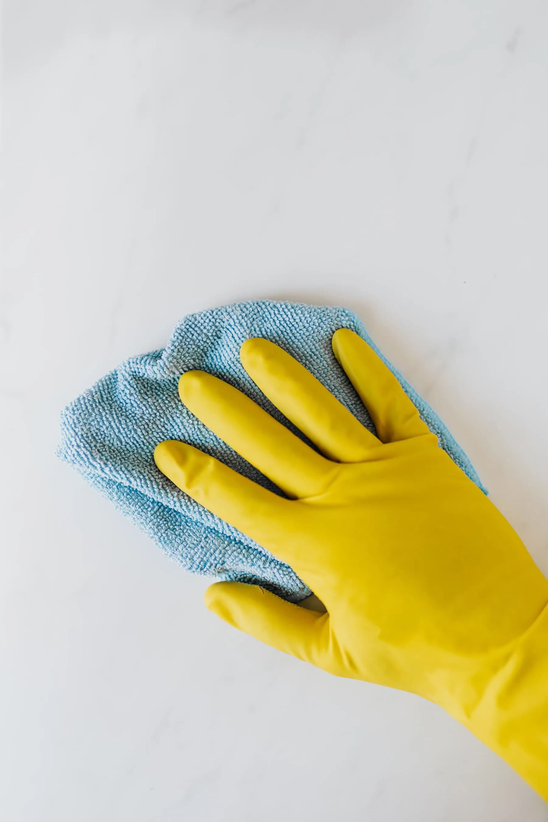 Hand in een huishoudhandschoen neemt een wit oppervlak af met een doek