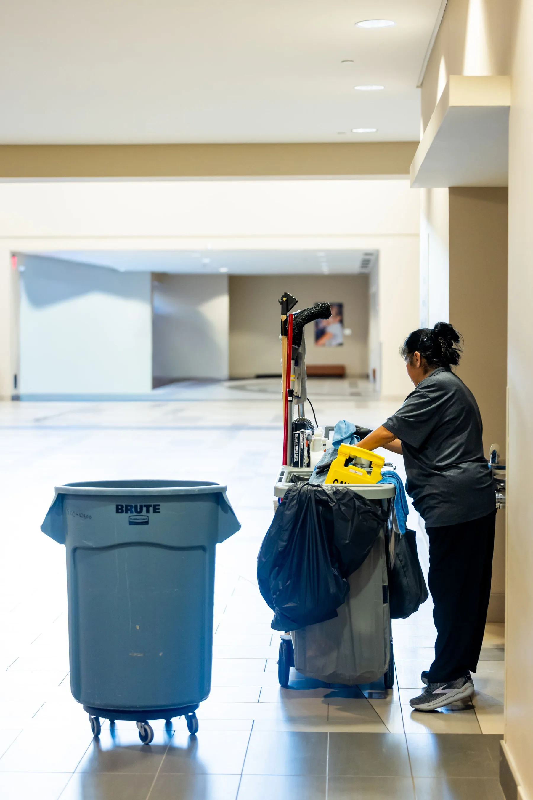 Schoonmaker met een schoonmaakkar in de lange, lichte gang van een groot gebouw